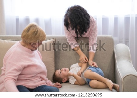 Grandmother and mother kissing baby boy on bed at home