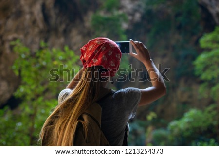 Girl tourist makes mobile photo by phone in tropical cave