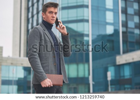 Young business man with notepad and mobile phone near of modern building.
