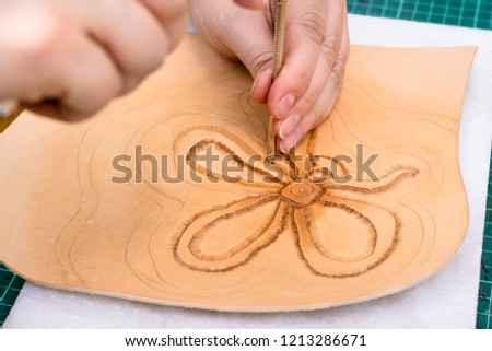 workshop of making the carved leather bag - craftsman stamps the relief drawing of flower on surface of rough vegetable tanned leather with Stamping tool close up