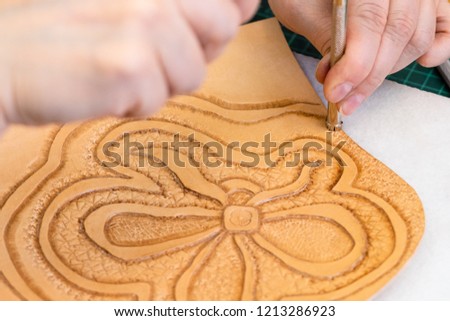 workshop of making the carved leather bag - craftsman stamps the relief picture of flower on surface of rough vegetable tanned leather with Stamping tool close up