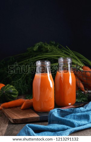 Carrot juice and carrot with leaves on black and wooden background