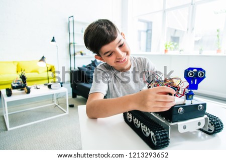 Cheerful ingenious boy constructing a robotic device while doing his home assignment Royalty-Free Stock Photo #1213293652