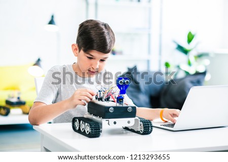Nice little boy using his laptop while experimenting with robotic technologies Royalty-Free Stock Photo #1213293655