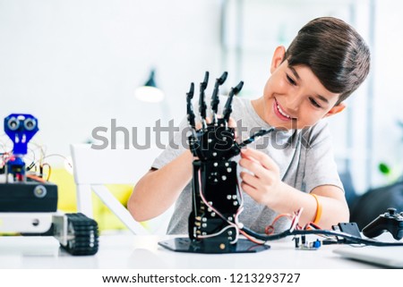 Joyful smart whizzkid experimenting with humanoid robotic hand while developing his skills Royalty-Free Stock Photo #1213293727