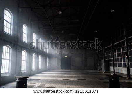 Sunlight shining throuh the windows of an old abandoned industrial warehouse building Royalty-Free Stock Photo #1213311871