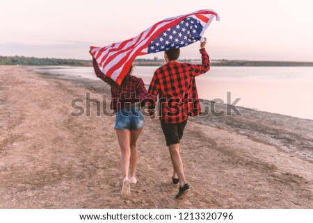 Happy young american couple on the beach waving american flag. Freedom and independence concept