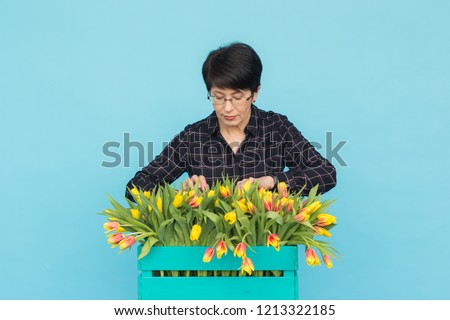 Happy middle-aged woman with glasses holding box of tulips in blue background