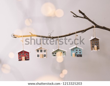 Beautiful festive new year and Christmas decorative little wooden houses hanging on a stick on the grey wall background, with fireflies glowing on the foreground Royalty-Free Stock Photo #1213325203