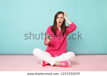 Full length portrait of young fun woman in rose shirt white pants sit on floor hold cellphone isolated on bright pink blue pastel wall background studio. Fashion lifestyle concept. Mock up copy space