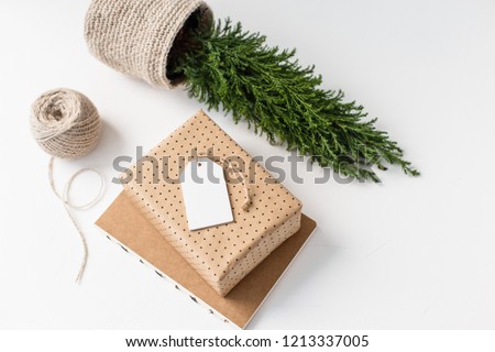 Small Christmas tree, cypress in a jute basket with notebook, wrapped gift and wooden white tag.