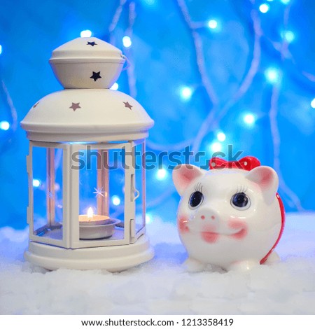 Christmas picture with candle light and symbol of 2019 new year pig with a red bow on the snow on a blue background with lights