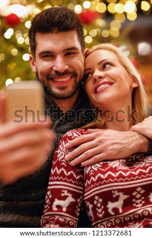 smiling woman and man in warm sweaters taking selfie picture with smartphone at home
