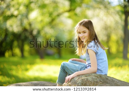 Adorable preteen girl in blooming apple tree garden on beautiful spring day. Cute child picking fresh apple tree flowers at spring.
