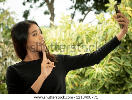 Young Thai girl taking a funny selfie with her smart phone outdoors