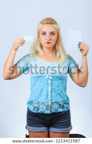 Serious cute girl in casual blue shirt and jeans shorts holds empty white signs, blank papers, business cards