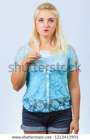 Young blonde girl in casual blue shirt holds blank business card with copyspace