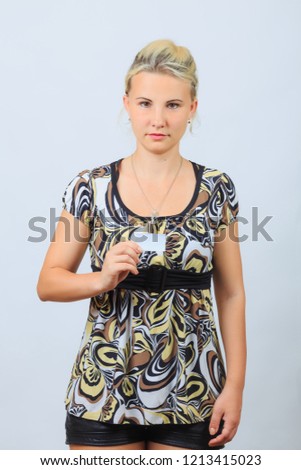 Young blonde girl in  casual shirt holds blank business card with copyspace