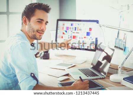 Portrait of young designer sitting at graphic studio in front of laptop and computer while working online.