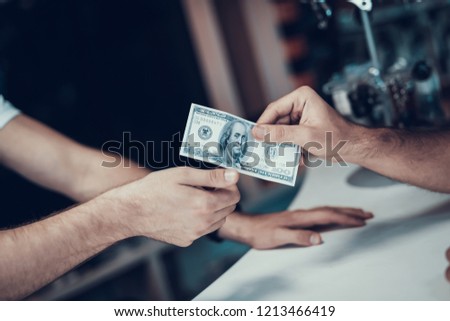 Closeup of Male Hand Gives Money From Purse to Seller. Shop Assistant Hand Takes Cash with Blurred Customers and Bikes on Backround in Sport Bicycle Store. Cash Payments Concept