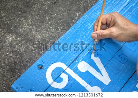 Writing signs board with a brush of watercolors on cement floor background. Painting on wooden board in thai language for advertising.
