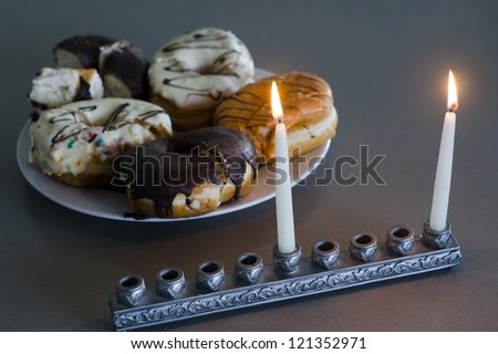 The first candle of Hanukkah with chanukiah and plate with donuts.