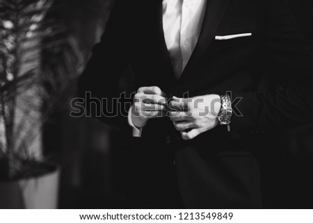 Fashion groom in trendy suit posing to photographer. Blond hair man with bow tie and other accsessories stand by the beautiful hotel