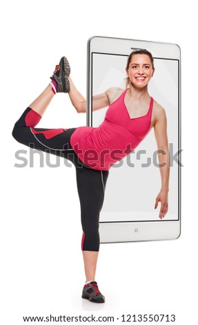 Young fit smiling woman doing stretching exercise with raised leg, concept virtual reality of the smartphone. going out of the device