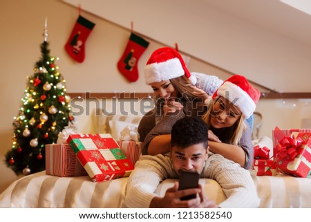 Friends posing for selfie on bed surrounded by Christmas presents. In background Christmas tree. Christmas holidays concept.