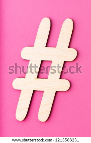Hashtag sign made of wooden material on pink background. Top view