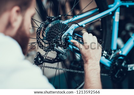 Bike Mechanic Repairs Bicycle in Workshop. Closeup Portrait of Young Blurred Man Examines and Fixes Modern Cycle Transmission System. Bike Maintenance and Sport Shop Concept