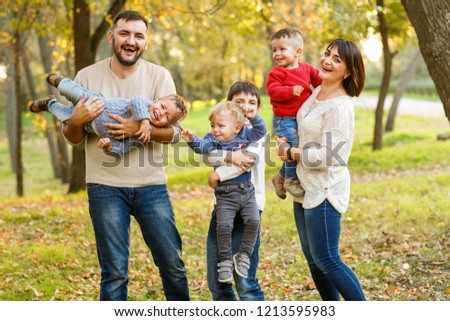 Lovely big family with four cheerful sons are playing on yellow autumn leaves in park Royalty-Free Stock Photo #1213595983