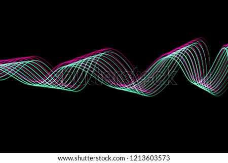 Long exposure, light painting photography.  Green and neon pink parallel lines of vibrant color, curving and wavy lines against a black background