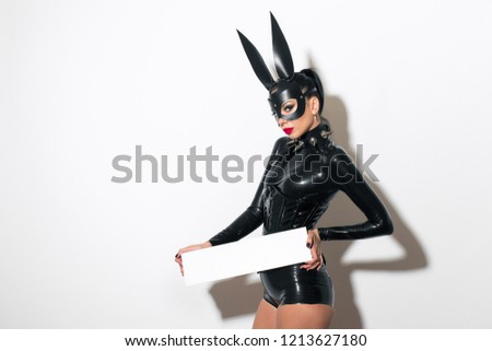 Beautiful dominant brunette vamp mistress bdsm girl with fashion makeup in glamour latex dress, corset, collar and bdsm black leather fetish rabbit mask posing on white background
