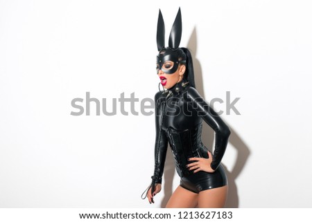 Beautiful dominant brunette vamp mistress bdsm girl with fashion makeup in glamour latex dress, corset, collar and bdsm black leather fetish rabbit mask posing on white background