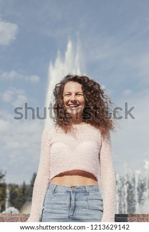 Outdoor shot of hot pinup woman in trendy pink top and denim skirt, laughing out load, smiling joyfully posing over park with fountain background, walking enjoying warm sunny day, taking pictures.