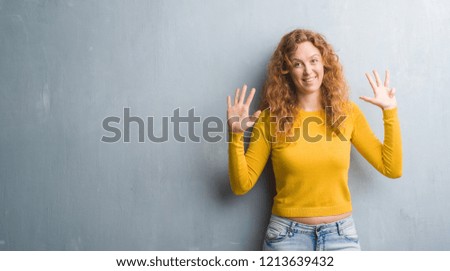 Young redhead woman over grey grunge wall showing and pointing up with fingers number nine while smiling confident and happy.
