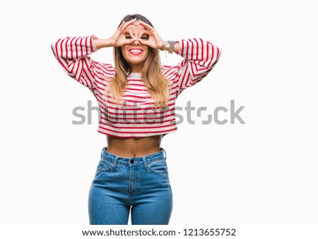 Young beautiful woman casual stripes winter sweater over isolated background doing ok gesture like binoculars sticking tongue out, eyes looking through fingers. Crazy expression.