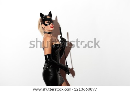 Beautiful dominant blonde vamp mistress bdsm girl with fashion makeup in glamour latex skirt, corset, collar and bdsm black leather fetish cat mask posing with whip on white background