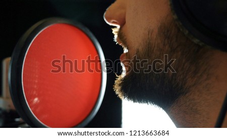 Mouth of male singer singing in sound studio. Unrecognizable man recording new song. Guy with beard sings to microphone. Working of creative musician. Show business concept. Slow motion Close up.