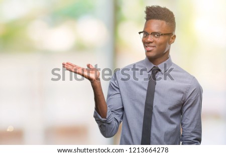 Young african american business man over isolated background smiling cheerful presenting and pointing with palm of hand looking at the camera.