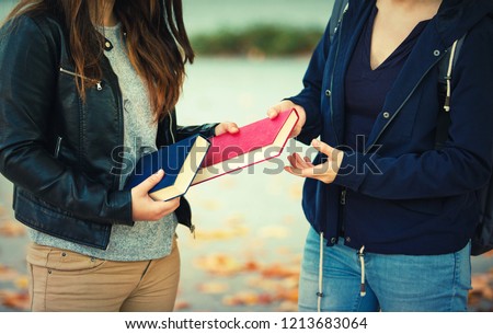 Close up outdoors portrait of two women students exchanging books. Knowledge sharing between people. Give to read to a friend. Royalty-Free Stock Photo #1213683064