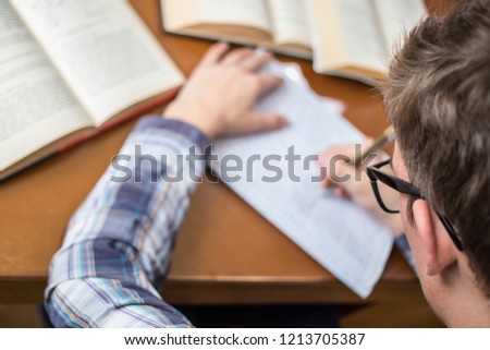 The student with glasses doing a homework, he writes in the workbook. Study learning concept.