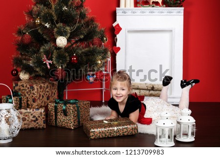 Little happy positive cheerful blondie caucasian girl prepearing to merry christmas near new year eve with gifts and presents from santa