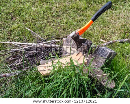 Ax and wood on the grass. Chopping wood, camp preparing. Male hard work. Summer, sunny day. Cracked tree stump with hatchet, gardening tools. Firewood. Rural photo for design, web, articles, sites