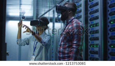 Side view of adult diverse man and woman wearing VR goggles and working in server room of data center