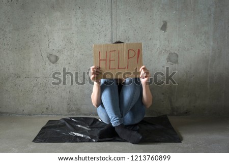 Young woman holding a poster with word Help against the concrete wall. 