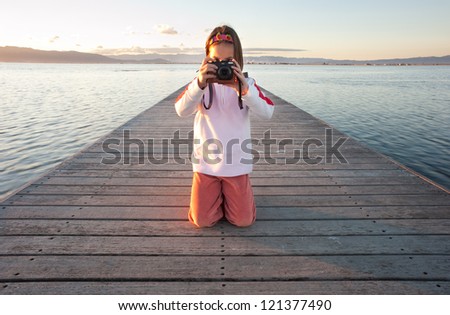 little girl taking a photograph on a pier