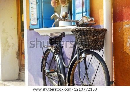 An old vintage bicycle with a headlamp and a basket is standing on the street near the open blue window, the theme of wallpaper and country style.
