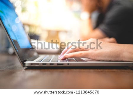 close up image of hand working and typing on laptop, computer keyboard on wood table, at cafe or coffee shop